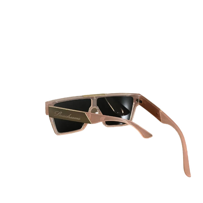 A pair of designer sunglasses with a translucent pink frame and dark lenses, resting on a dark wooden table. The brand name 'Dior' is visible in gold script on the temple arm.