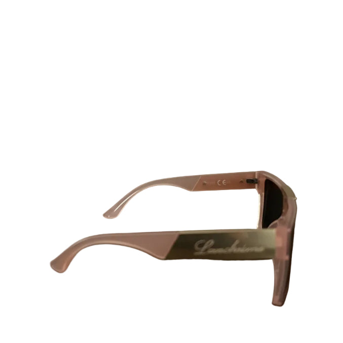 Pink acetate sunglasses with dark lenses resting on a dark wooden table, with a domestic room background showing a door and wall socket.
